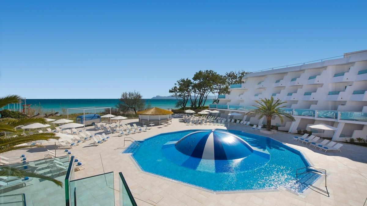 Außenbereich des Iberostar Playa de Muro Hotels mit Pool und Sonnenliegen.