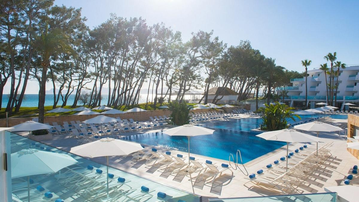 Außenbereich des Pools im Iberostar Playa de Muro Hotel mit vielen Liegestühlen und Sonnenschirmen.