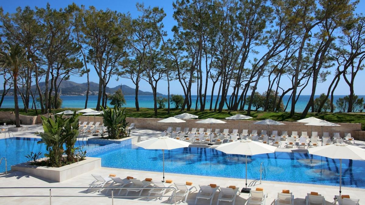 Außenpoolbereich des Iberostar Playa de Muro Hotels mit weißen Sonnenliegen und Schirmen.