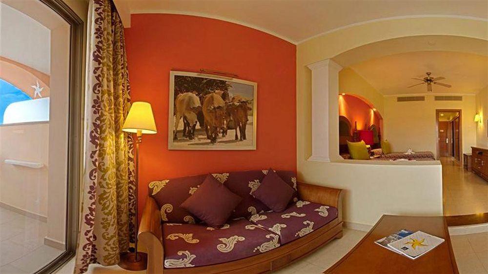 Wohnbereich im Iberostar Selection Rose Hall Suites Hotel mit einem Sofa, einem Tisch und einem Bild an der Wand.