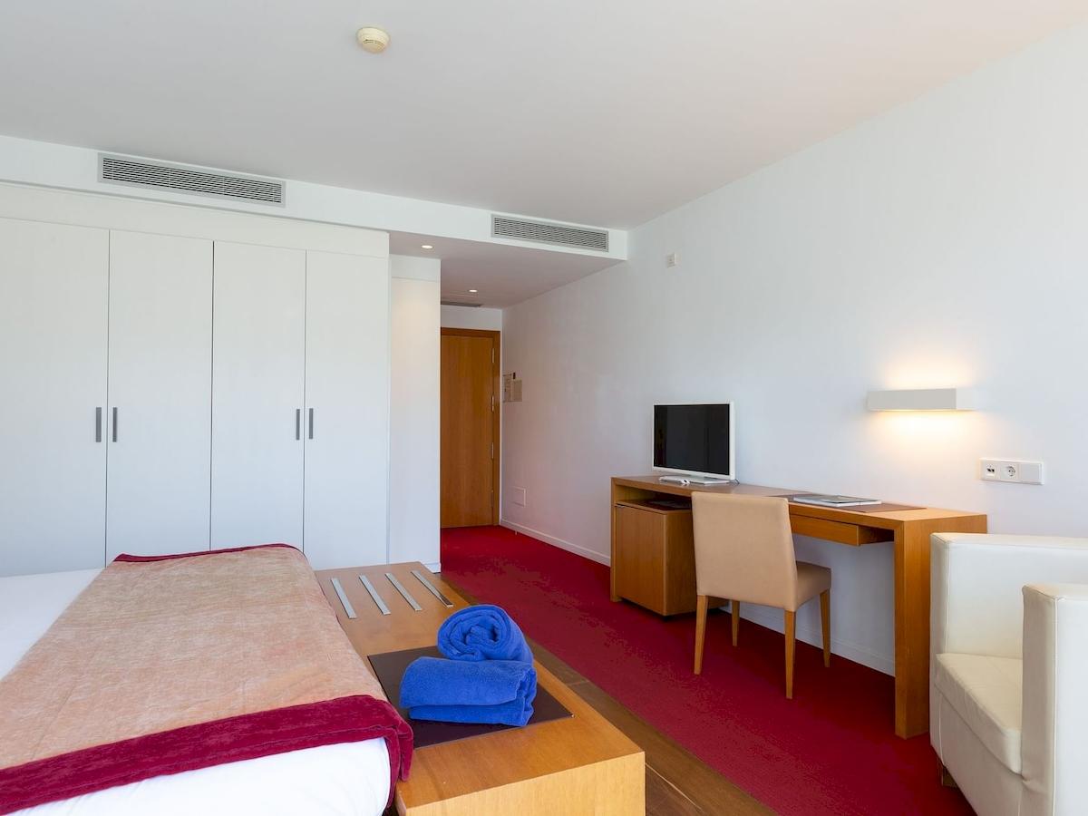 Innenansicht eines Hotelzimmers im Aimia Hotel mit Bett, Schreibtisch und roten Teppich