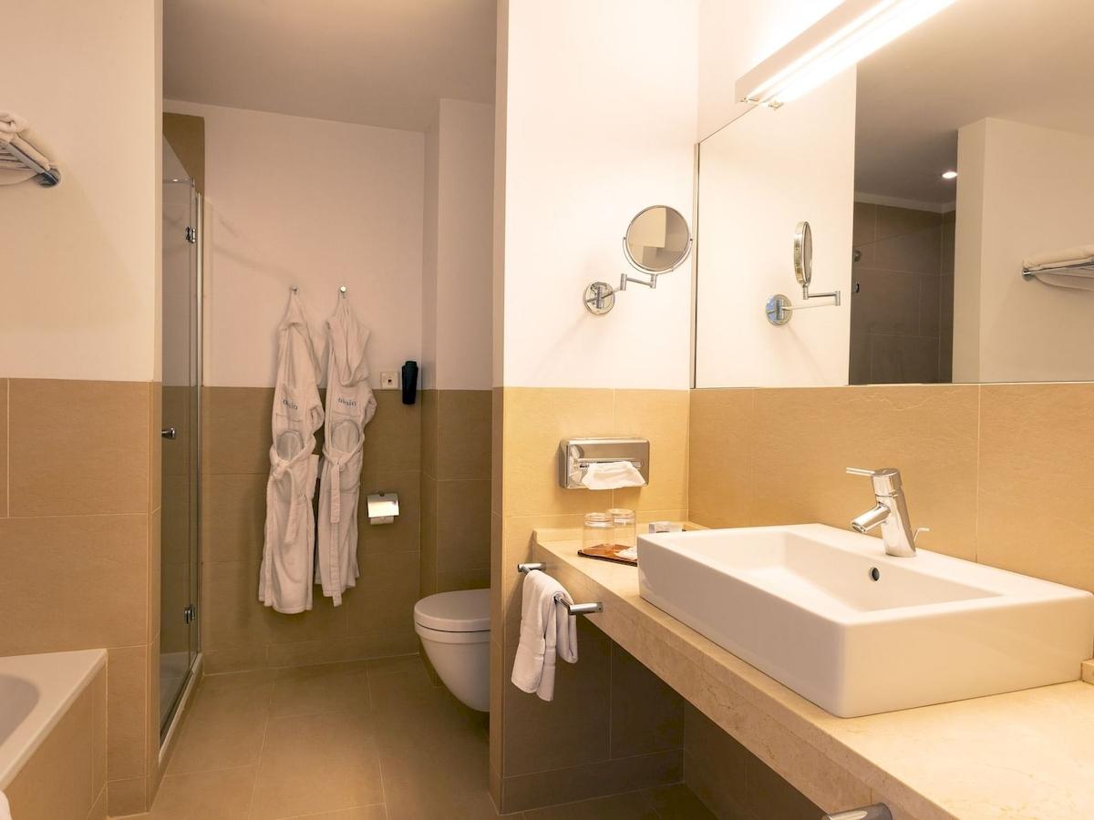 Badezimmer im Aimia Hotel mit Badewanne, Toilette, Waschbecken und Spiegeln.