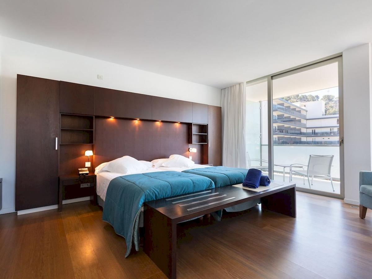 Schlafzimmer im Aimia Hotel mit zwei Betten, dunklem Holzboden und großen Fenstern.
