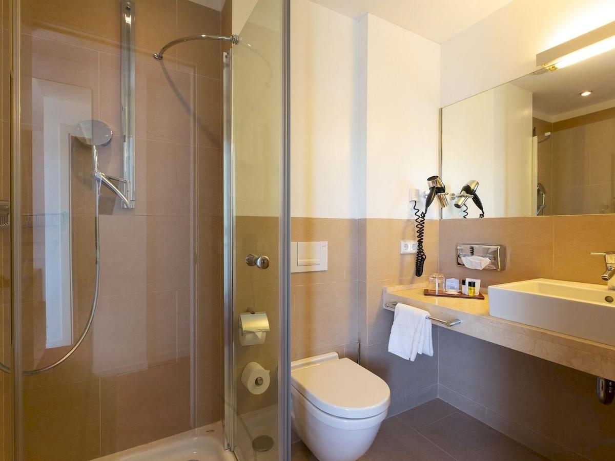 Badezimmer im Aimia Hotel mit Dusche, Toilette und Waschbecken.