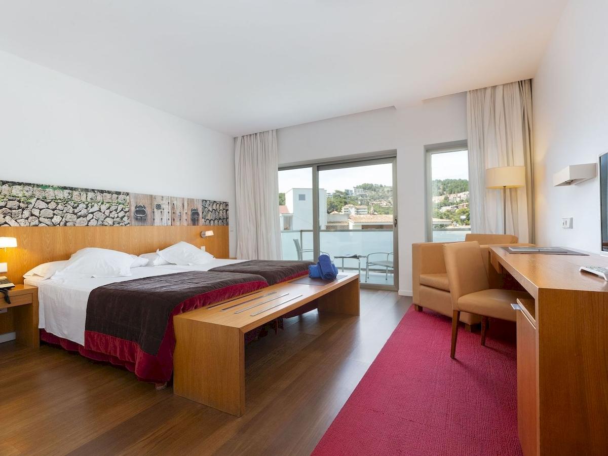 Hotelzimmer im Aimia Hotel mit zwei Betten, Balkon und Schreibtisch.