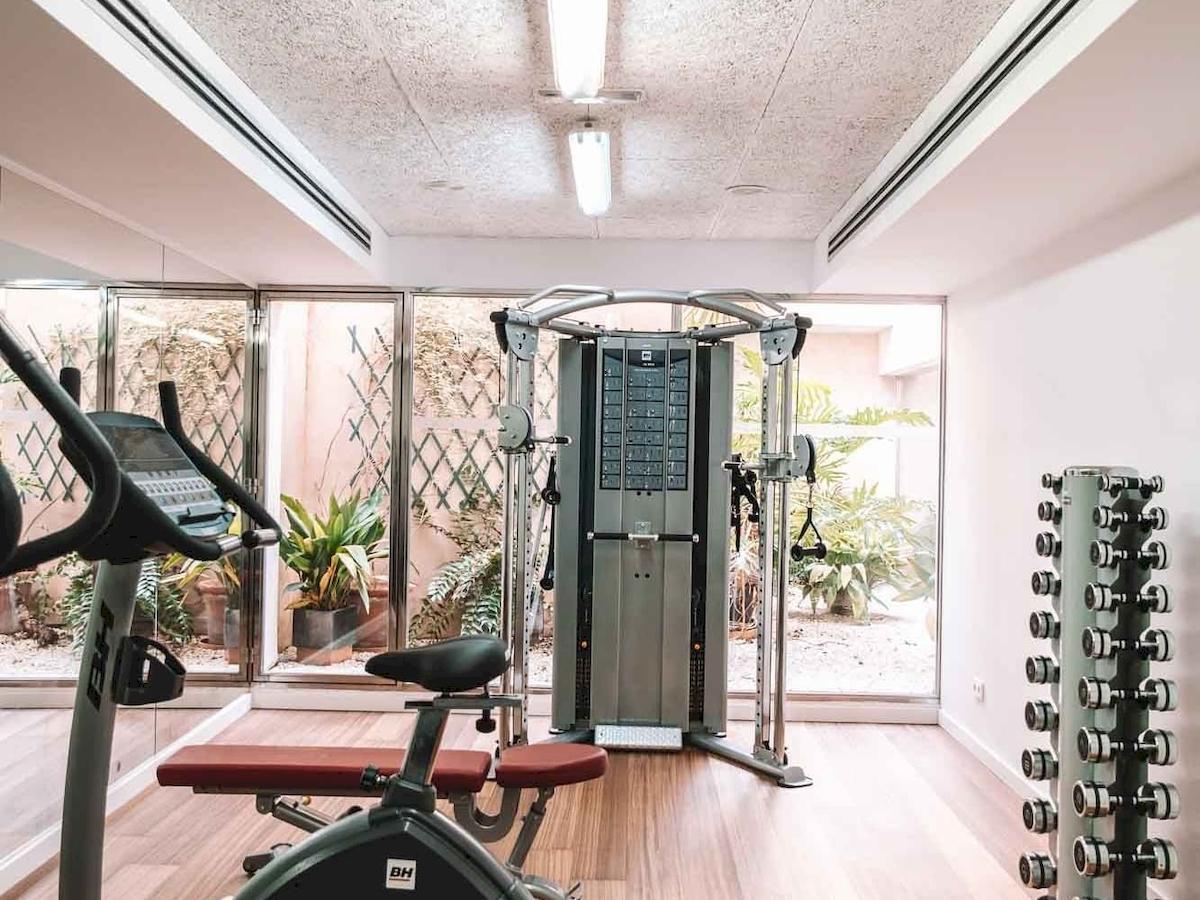 Fitnessbereich des Aimia Hotels mit Geräten und Blick auf Pflanzen.