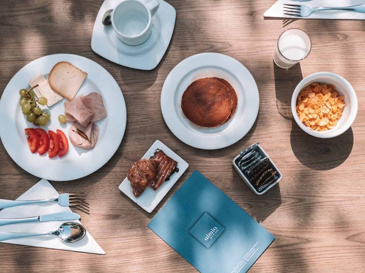 Frühstücksbuffet im Aimia Hotel mit verschiedenen Gerichten und Getränken auf einem Holztisch.