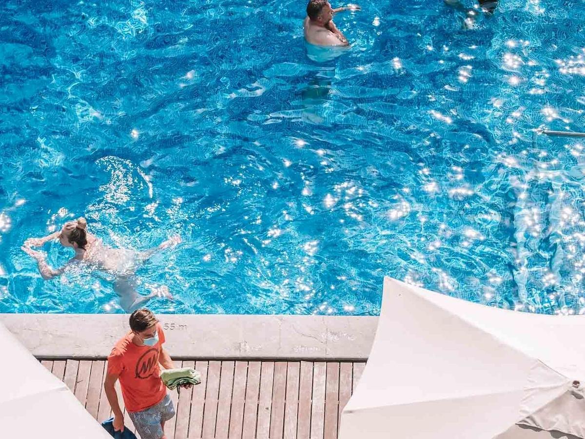 Aussicht auf das Schwimmbad des Aimia Hotels mit Gästen, die schwimmen und einer Person, die Handtücher hält.