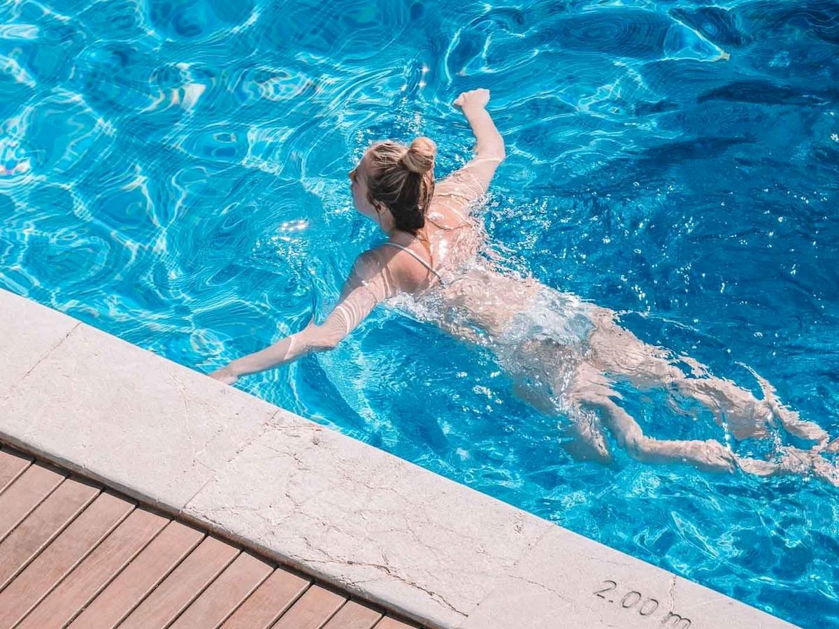 Frau schwimmt im blauen Pool des Aimia Hotels