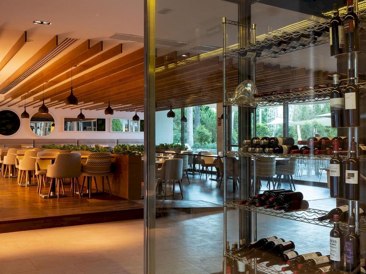 Innenansicht des Restaurants im Aimia Hotel mit Tischen, Stühlen und Pflanzen in der Mitte.