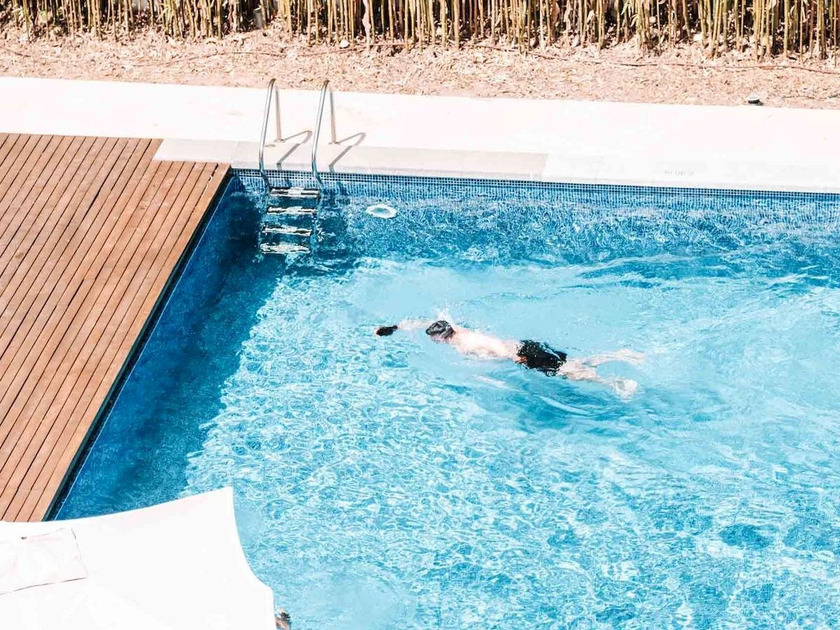 Ein Schwimmer im Pool des Aimia Hotels, umgeben von einer hölzernen Terrasse und einer Treppe.