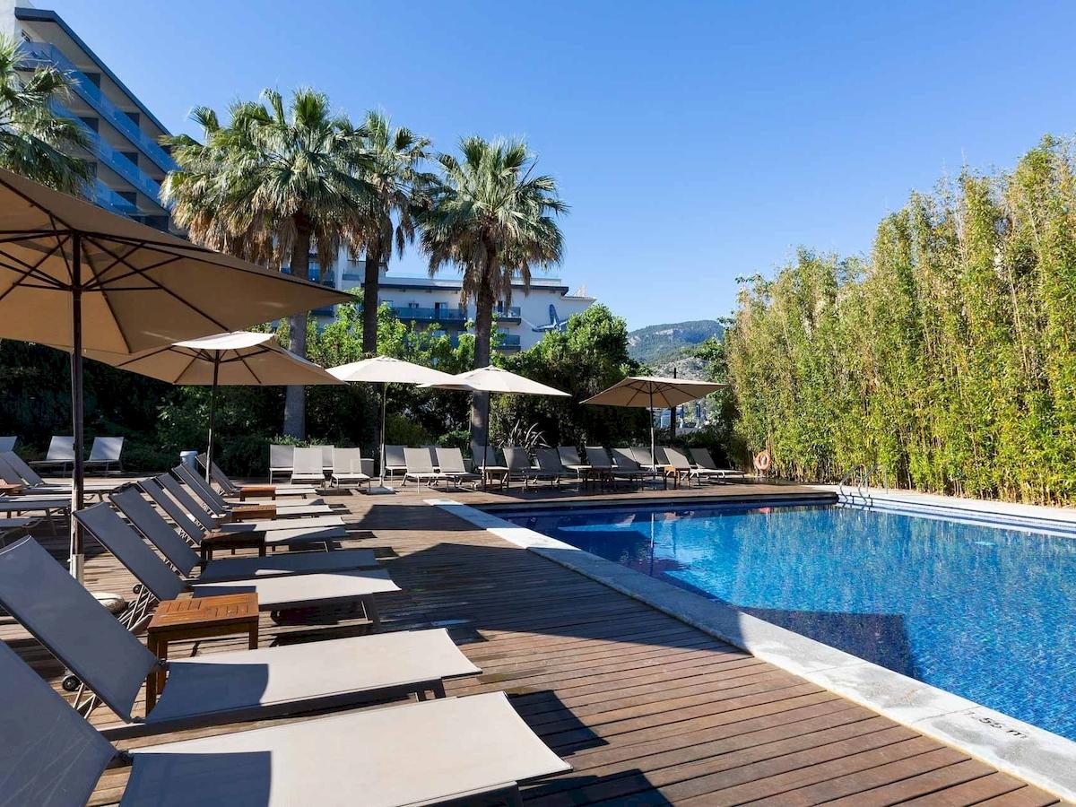 Außenpool mit Liegen und Sonnenschirmen neben dem Aimia Hotel