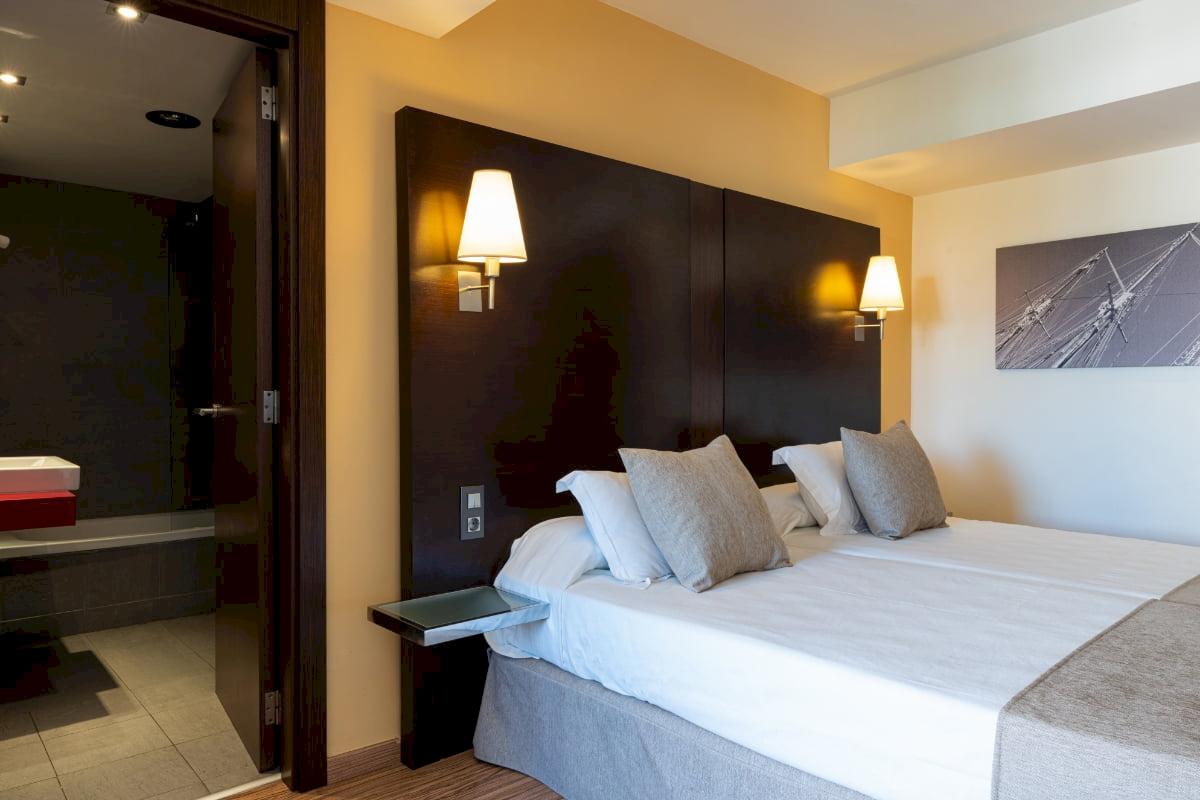Doppelbett im Hotelzimmer des Nautic Hotel & Spa mit Nachttisch und Lampen.
