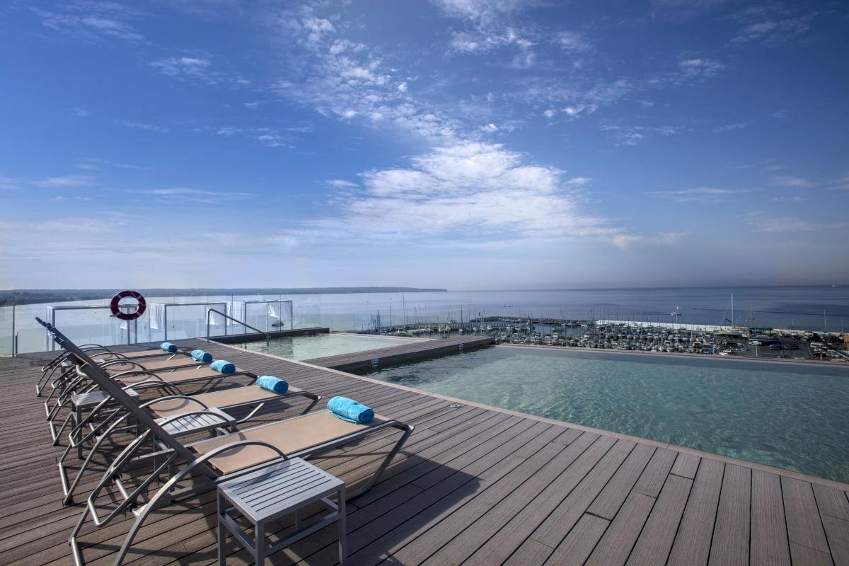 Dachterrasse des Nautic Hotel & Spa mit Infinity-Pool und Meerblick, Liegen und Handtüchern.