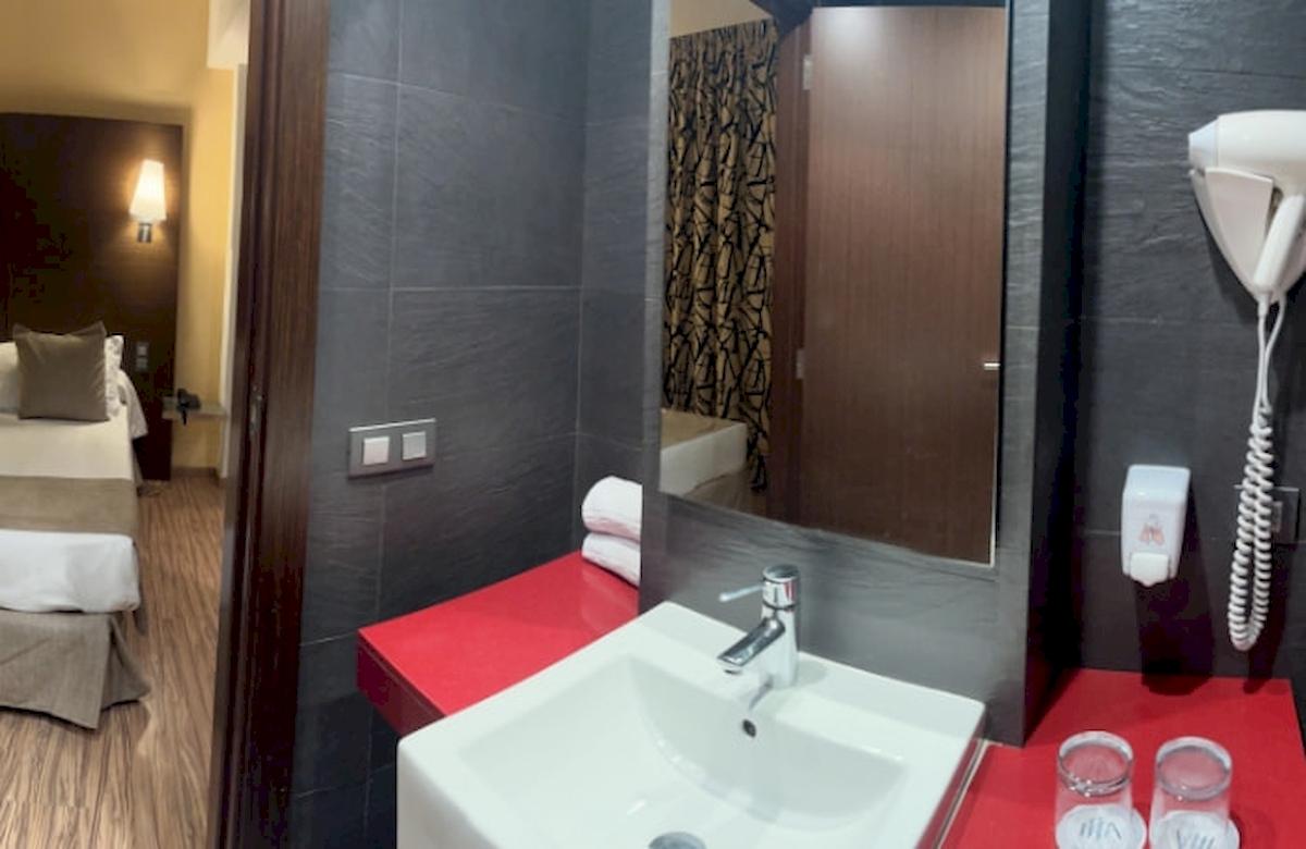 Badezimmer im Hotelraum mit Bett und Spiegel, Handtuchhalter und Föhn.