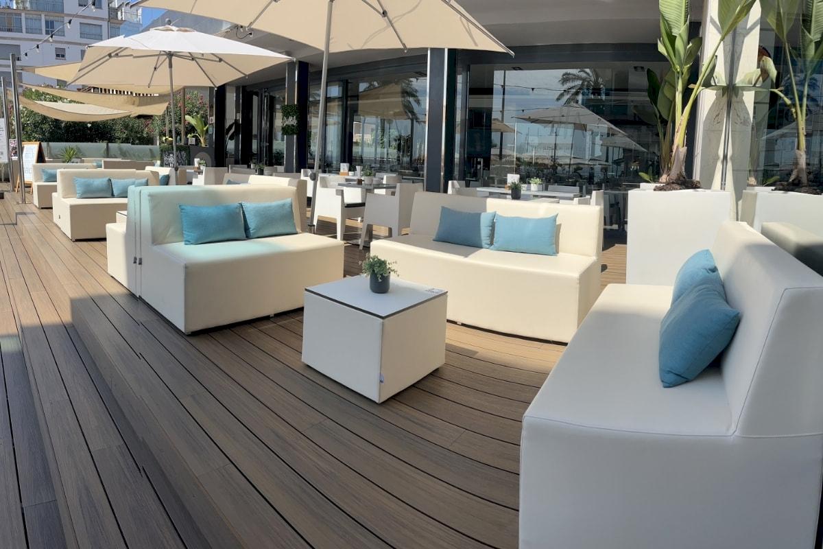 Terrasse des Nautic Hotel & Spa mit weißen Sofas und Tischen, blauen Kissen und großen Sonnenschirmen.