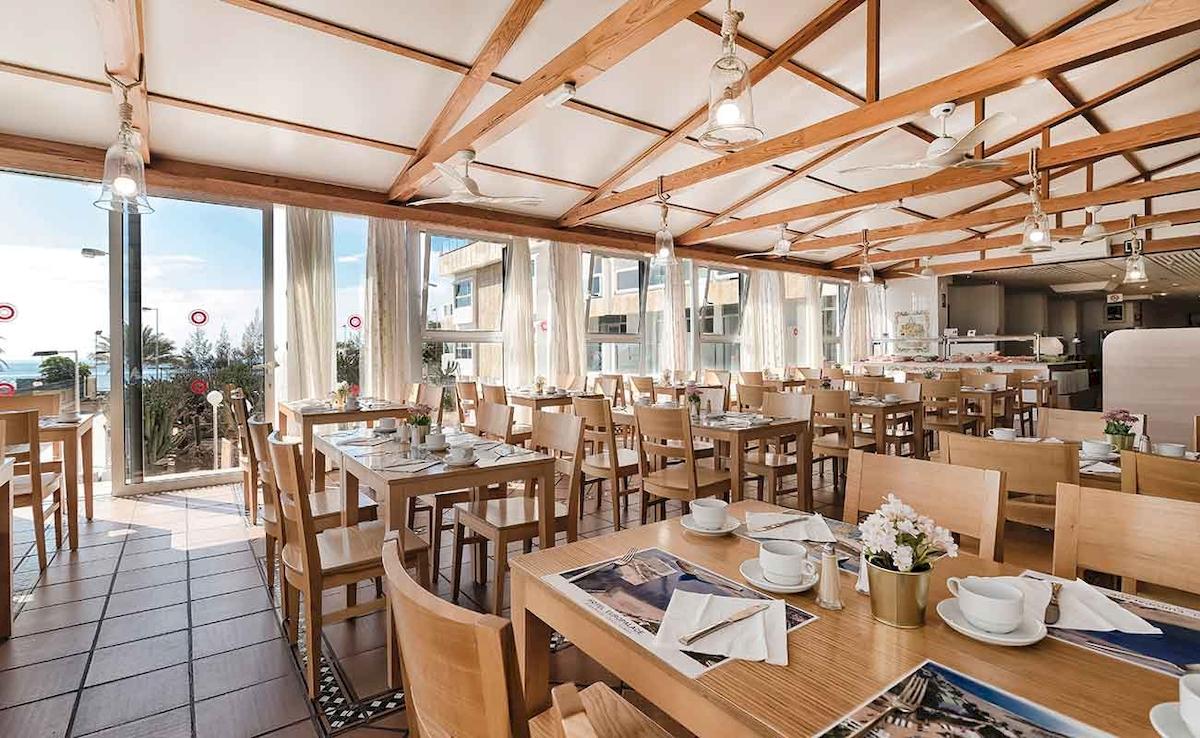 Foto des Innenraums des Restaurants im Europalace Hotel mit Holztischen und Stühlen, Tischblumen und Fenstern mit Blick auf das Meer.