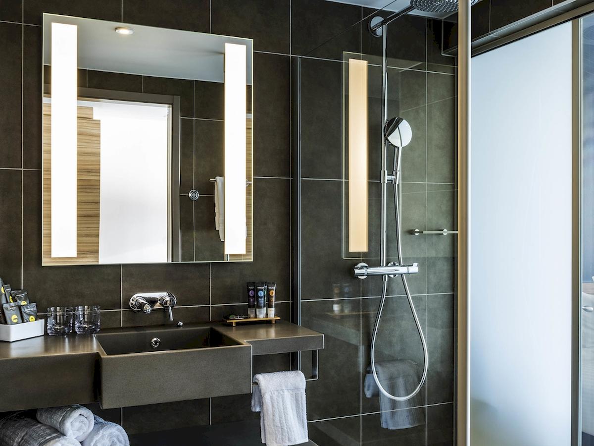 Badezimmer des Novotel London Canary Wharf mit Waschbecken, Spiegel und Dusche.