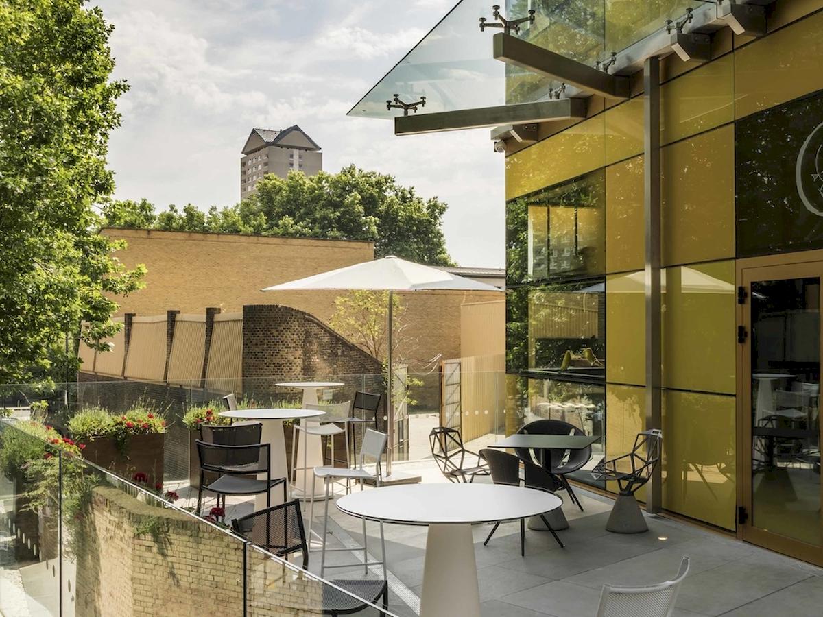 Terrasse des Novotel London Canary Wharf mit Tischen, Stühlen und Schirmen.