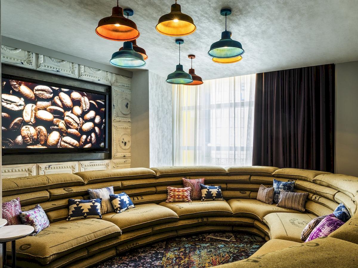 Lobby-Lounge des Novotel London Canary Wharf mit großer Couch und Kaffeebohnen-Bildschirm.