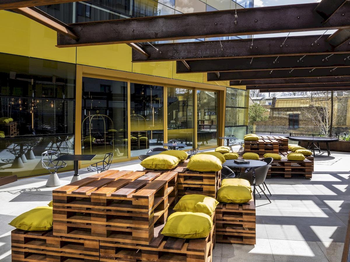 Terrasse des Novotel London Canary Wharf mit gelben Kissen und Holzpalettenmöbeln.