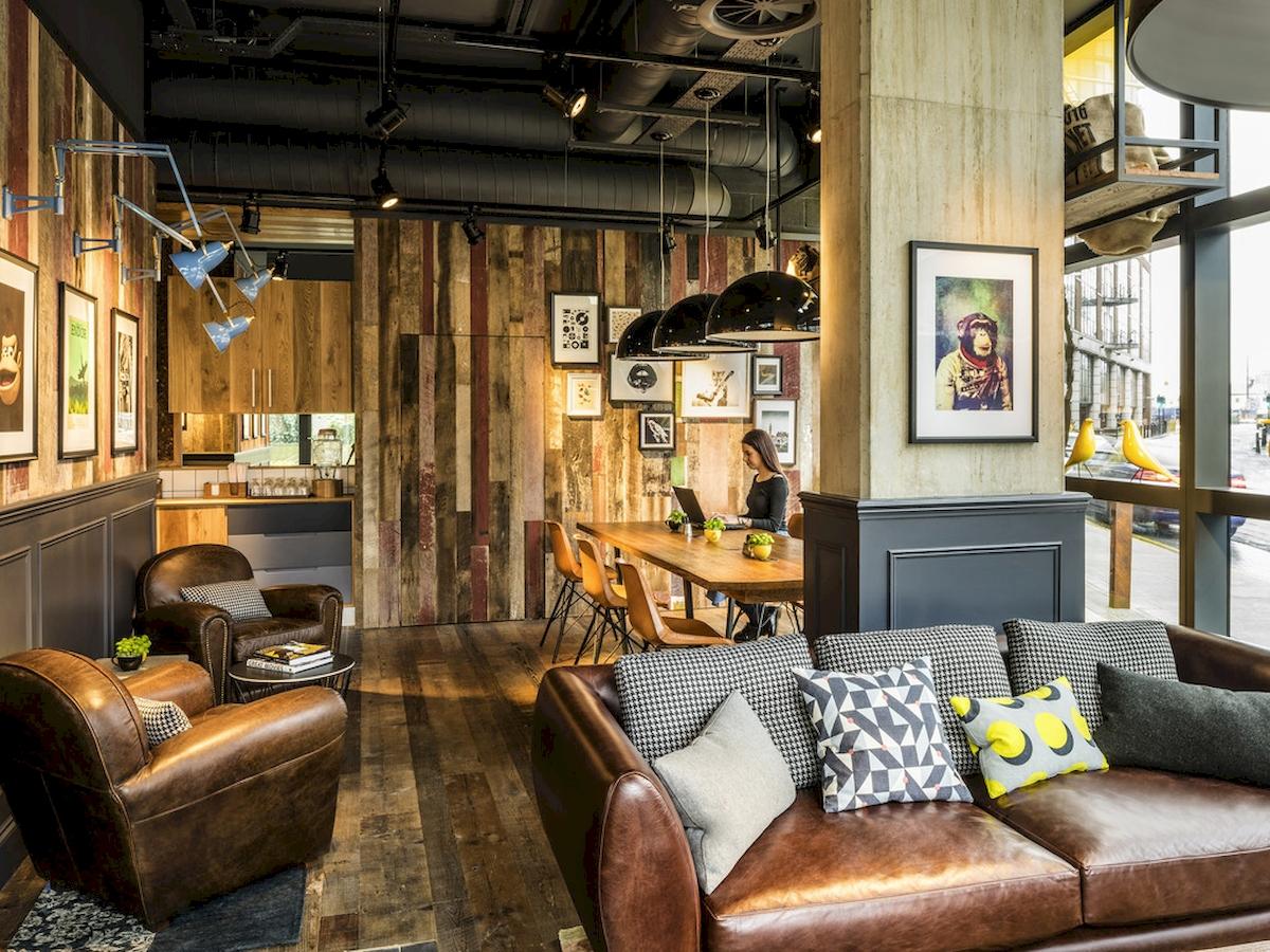 Inneneinrichtung des Novotel London Canary Wharf Hotel mit Ledersofa, Tisch und Frau am Laptop.