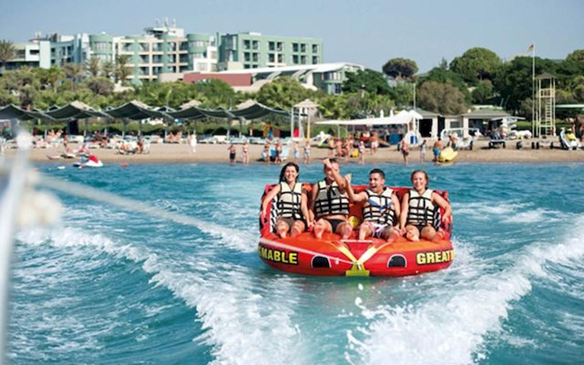 Vier Personen sitzen auf einem roten Schlauchboot und werden am Strand gezogen, vor dem Limak Atlantis Deluxe Hotel & Resort.