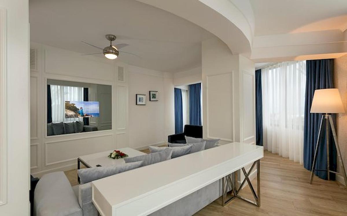Hotelzimmer-Innenraum mit weißem Sofa, Tisch, Fernseher, Lampe und Holzboden.