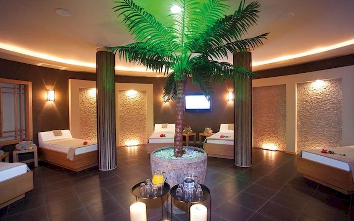 Innenansicht einer Suite im Limak Atlantis Deluxe Hotel & Resort mit Betten, einer Palme und einer Fernsehwand.