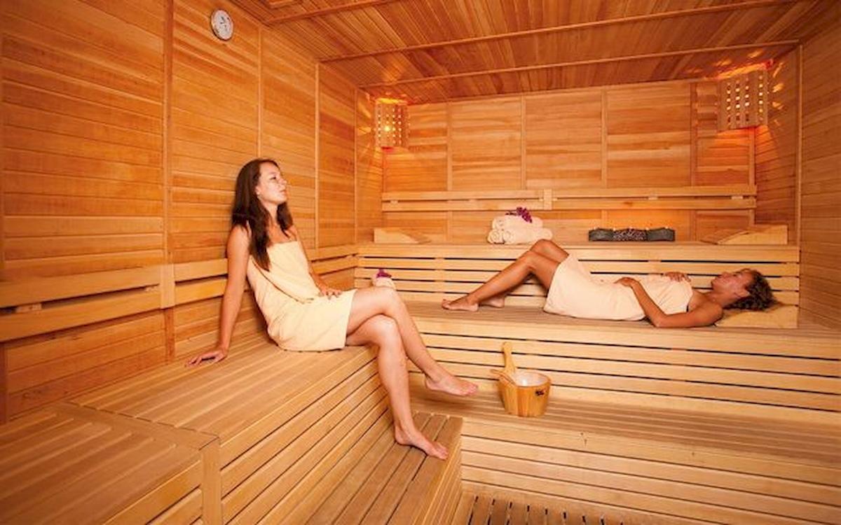 Zwei Frauen sitzen in einem Holzsauna, eine entspannt sich und die andere schaut zur Seite.