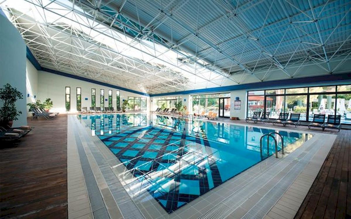 Innenansicht des Schwimmbades im Limak Atlantis Deluxe Hotel & Resort mit Liegestühlen und Glaswänden.