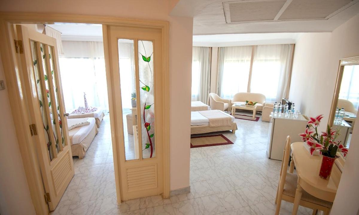 Innenansicht des Grand Hotel Hurghada mit Schlafzimmer, Bett, Tisch, Stuhl und Vase mit Blumen.