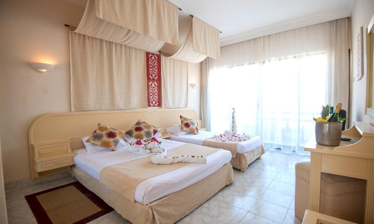 Doppelzimmer im Grand Hotel Hurghada mit zwei Betten, Dekor und einem Fenster mit Vorhängen.