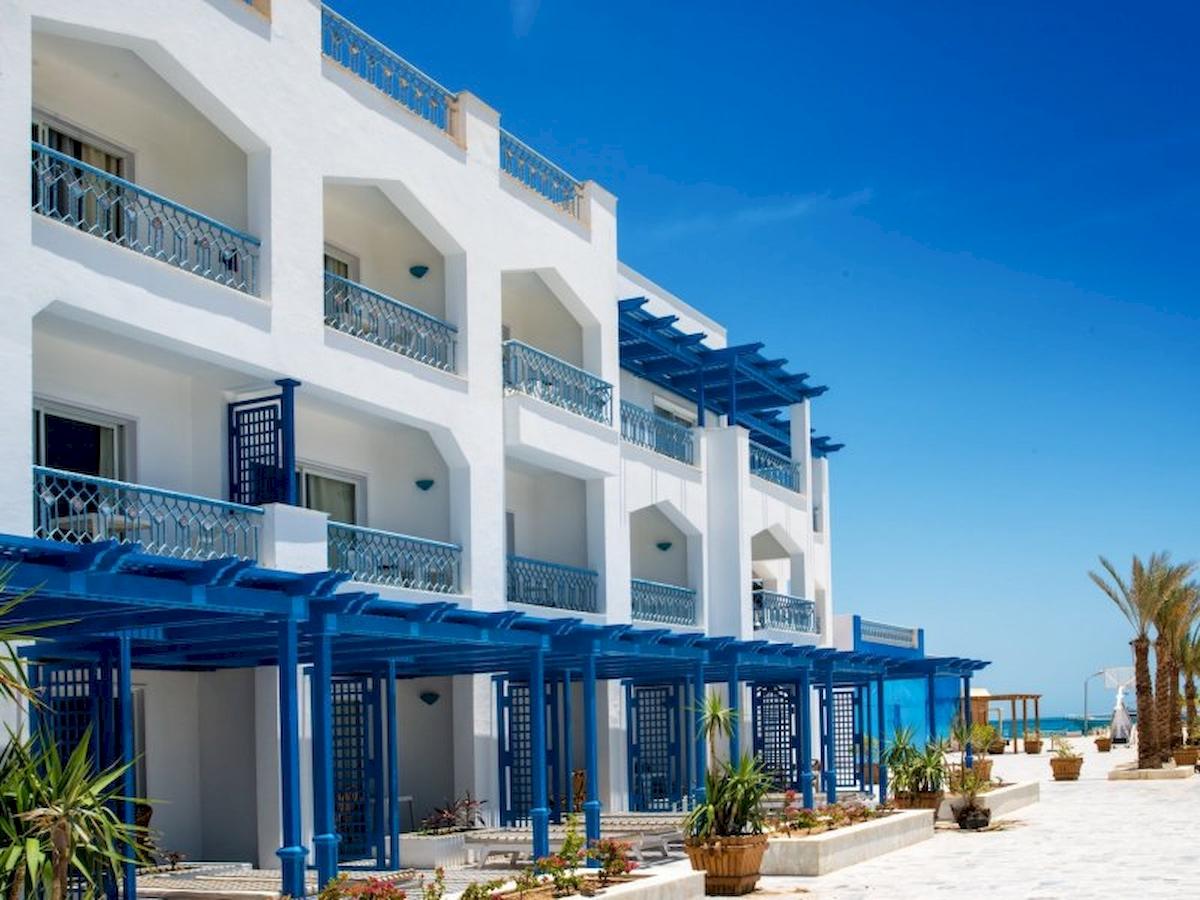 Außenansicht des The Grand Hotel Hurghada mit weißen Gebäuden und blauen Balkonen am Strand.