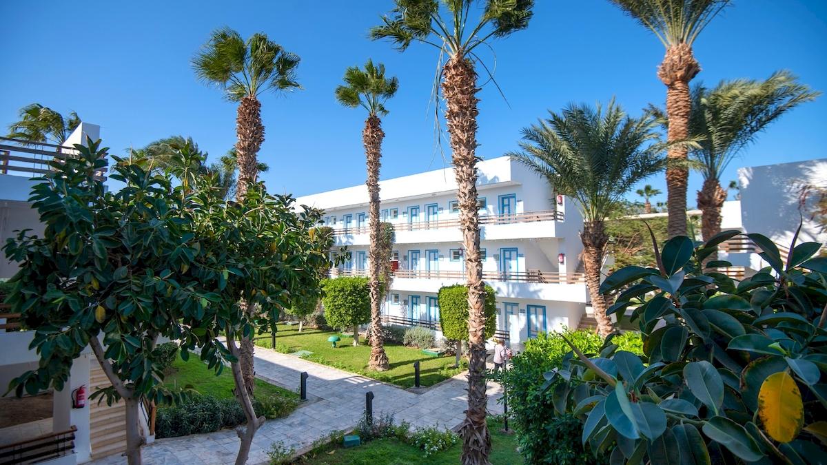 Außenansicht des Grand Hotel Hurghada mit weißen Gebäuden und blauen Fensterrahmen.