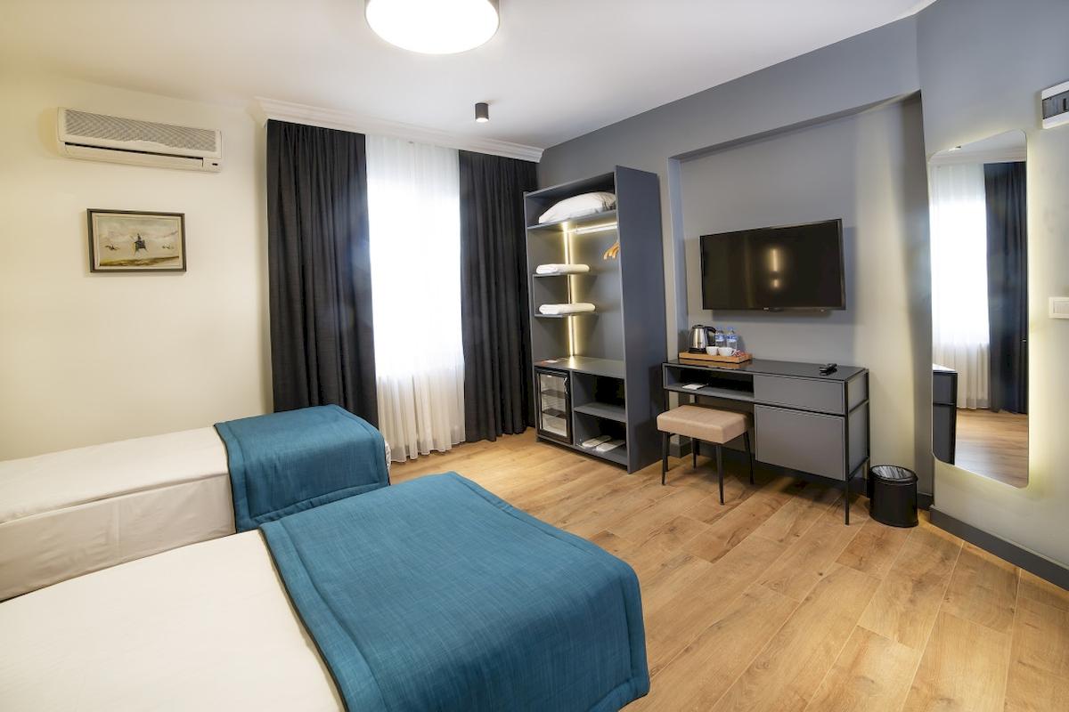 Innenansicht eines Hotelzimmers im Barin Hotel mit zwei Betten, einem Fernseher und einem Schreibtisch.
