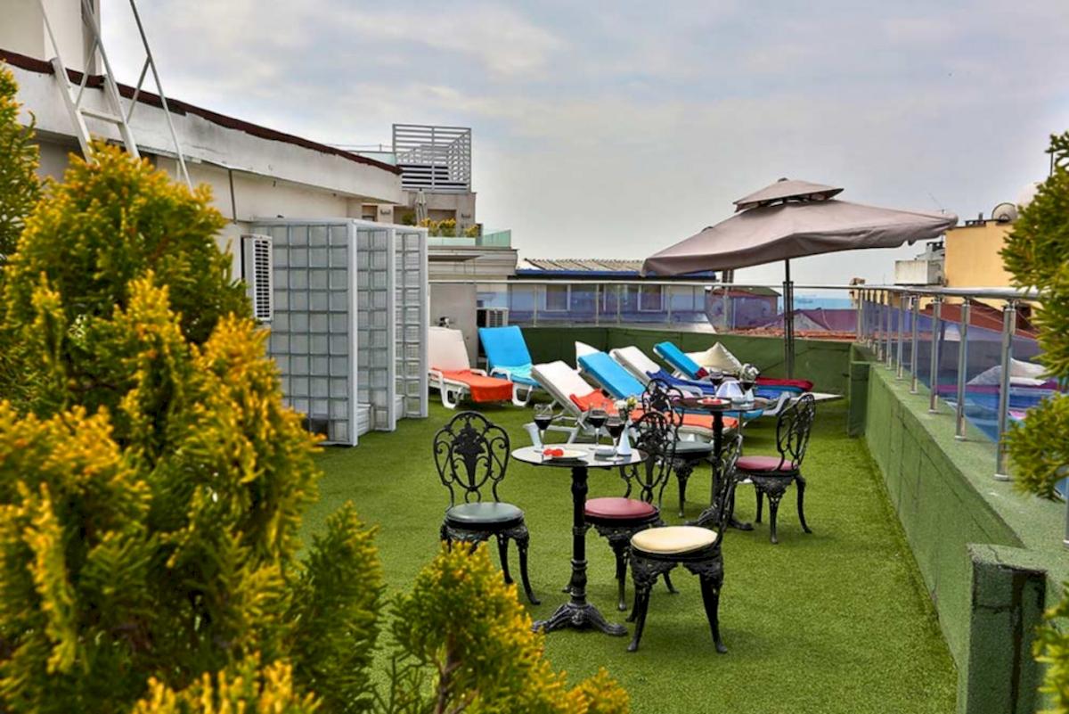 Dachterrasse des Barin Hotels mit Liegen, Tischen und einem Schirm.