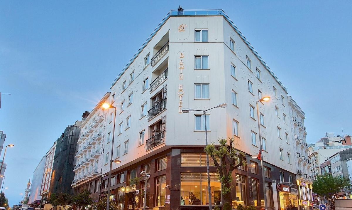 Außenansicht des Barin Hotels bei Nacht, ein weißes Gebäude mit vielen Fenstern und leuchtenden Straßenlaternen.