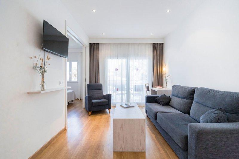 Wohnzimmer des Princesa Playa Hotels mit einem Fernseher an der Wand, einem Sofa, einem Stuhl und einem Tisch.