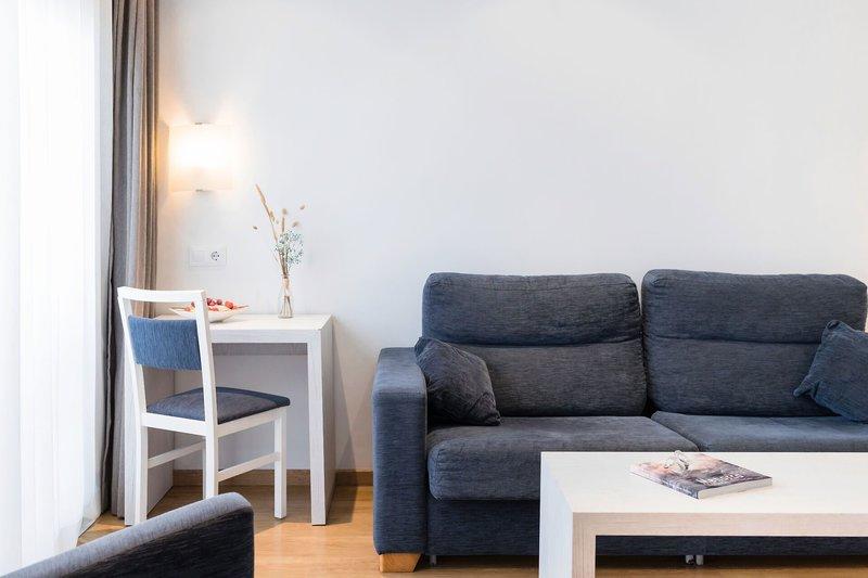 Wohnzimmer im Hotel Princesa Playa mit grauem Sofa, Tisch und Stuhl.