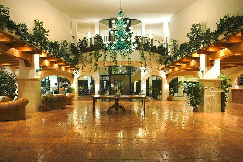 Empfangsbereich des Royal Son Bou Family Club Hotels mit grüner Kristallleuchte und Pflanzen.