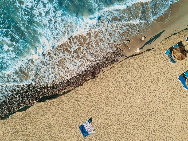 Oberflächenaufnahme von einem Strand mit Wellen und Sonne, mit Liegen und Handtüchern.