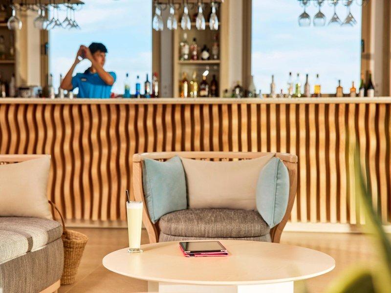Innenansicht der Bar im Victoria Menorca Hotel mit Barkeeper, Getränken und Möbeln.