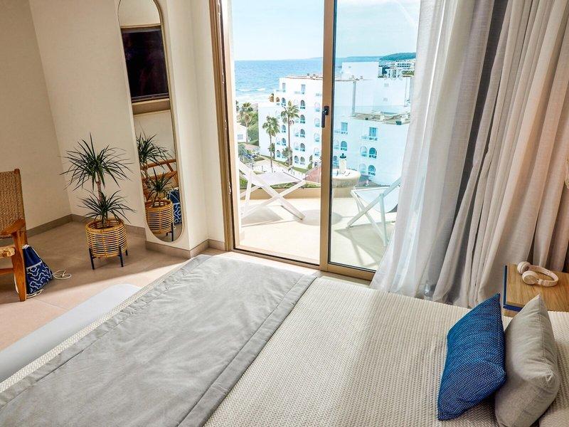 Schlafzimmer mit Meerblick im Victoria Menorca Hotel, mit Bett, Balkon, Pflanzen und Ausblick auf das Meer.