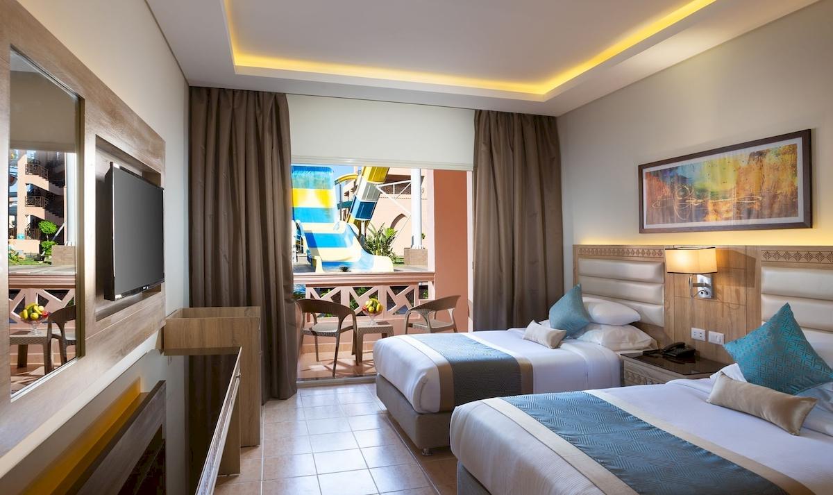 Doppelzimmer mit Balkon im Pickalbatros Aqua Park Resort - Hurghada, zeigt zwei Betten, Fernseher und einen Balkon mit Blick auf eine Wasserrutsche.