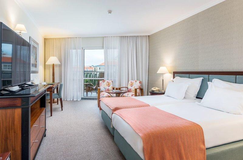 Hotelzimmer im Pestana Grand Premium Ocean Resort mit zwei Betten, Fernseher, Schreibtisch und Balkon.