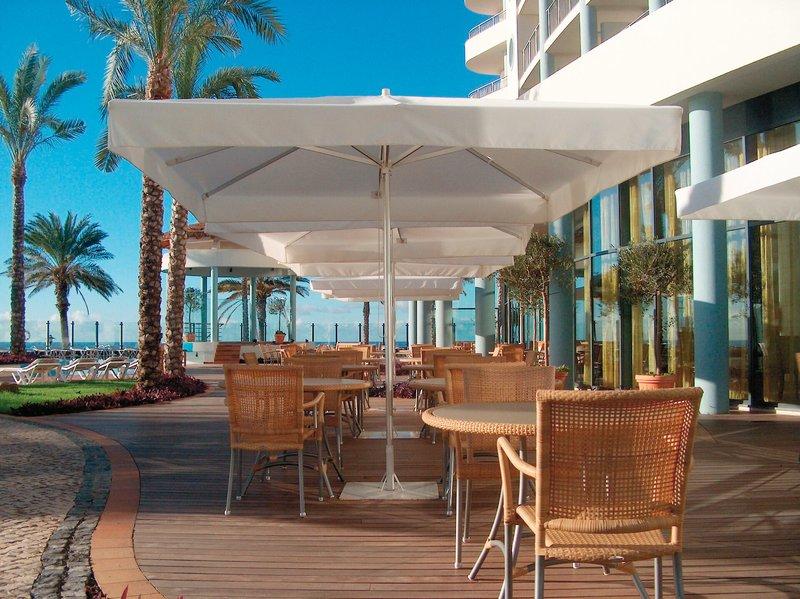 Terrasse des Pestana Grand Premium Ocean Resort mit Tischen und Stühlen unter weißen Sonnenschirmen.