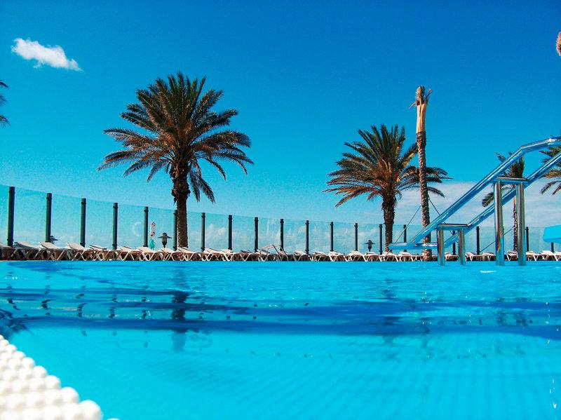 Ein blauer Swimmingpool im Pestana Grand Premium Ocean Resort mit Palmen und Sonnenliegen