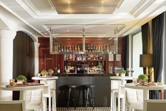 Innenansicht der Bar der Villa Marquis Melia Collection mit weißen Tischen, Stühlen und einer Theke.