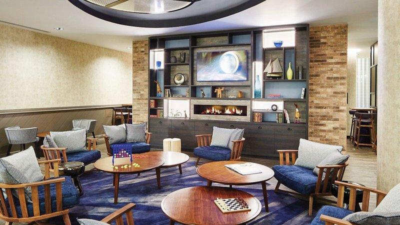 Hotel-Lounge mit Sofas, Tischen und einem Fernseher an der Wand.